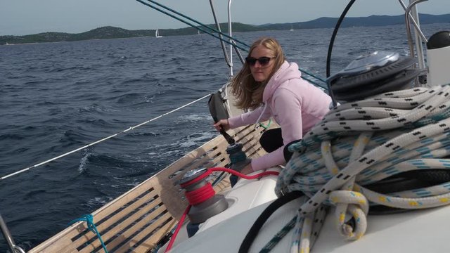 Blond girl on a sailboat. Skipper crew member winching sail ropes.