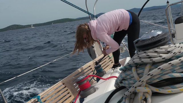 Young attractive girl winching the sail rope on a sailboat.