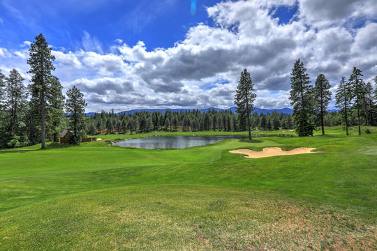 Golf course with pine trees and pond in cascade mountains of Northwest with little house.