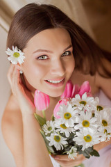 Obraz na płótnie Canvas Portrait of young beautiful woman holding flowers in hand and smiling. Closeup of tender happy girl posing with bouquet of tulips and daisies. Naked girl celebrating 8 march, women's or mother's day