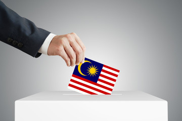 Man putting a voting ballot into a box with Malaysian flag.