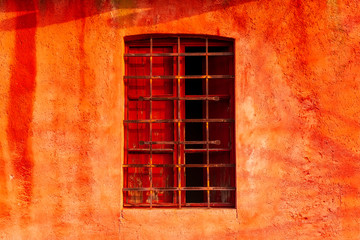 Vecchia finestra con un balcone chiuso e sbarre di casa rossa e abbandonata. 