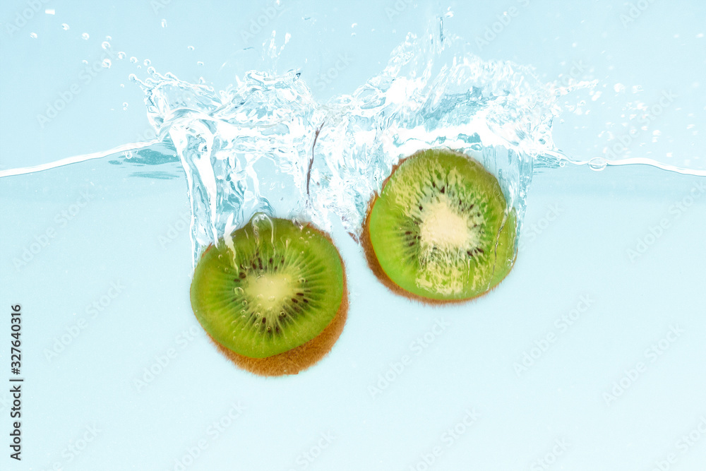 Poster fresh kiwi halves dropping into clear water with splashes on blue background