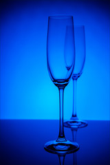 Two empty champagne glasses with reflection, on dark blue and black background gradient background. Concept, party and club life. Magazine and commercial photo with place for text or design, festival