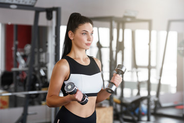 Fototapeta na wymiar Sports training. Young woman with dumbbells working out in gym