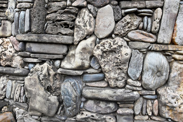 Gray stones of different sizes and shapes are laid out in a blank fence. Beautiful masonry made of flat, round gray and brown canoes.