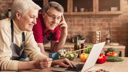Smiling elderly couple with laptop and credit card in kitchen