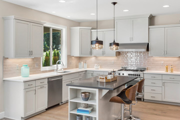 Bright and light kitchen in new home, with large island, stainless steel appliances, and hardwood floors