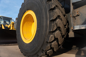 Fototapeta na wymiar Close up of huge tire and yellow rim of a bulldozer for excavating. Shallow depth of field with another machine in background with blue sky. 