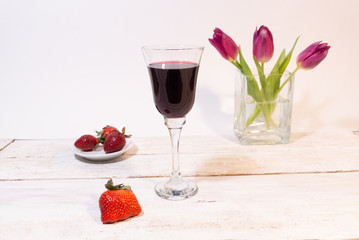 glass of red wine, red berry, strawberry on plate, pink tulips in vase on white background