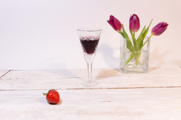 Vintage cristal glass of red wine, raspberry, pink tulips in vase on white background