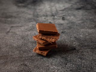 Broken pieces of coffee chocolate pyramid close up on gray stone background.