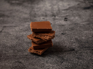 Stack of broken coffee chocolate pieces close up on gray stone background.