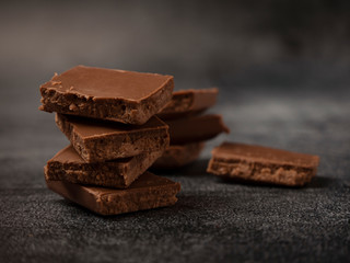 Stack of broken coffee chocolate pieces close up on gray stone background.