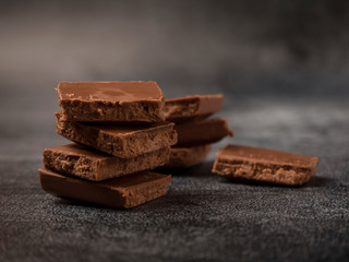 Stack of broken coffee chocolate pieces close up on gray stone background.