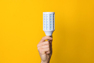 closeup hand holding white led lighting bulb against a yellow wide background. concept of idea,...