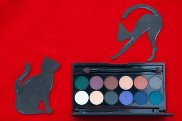 Makeup flat lay on the red background. Multicolored eye shadow and stencils in the form of a cat...
