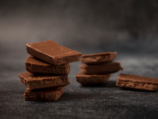 Stack of broken coffee chocolate pieces close up on gray stone background.
