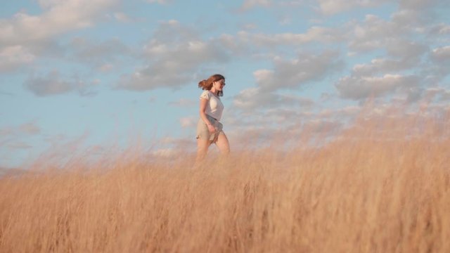 Young woman walking through yellow field at golden hour, slow motion