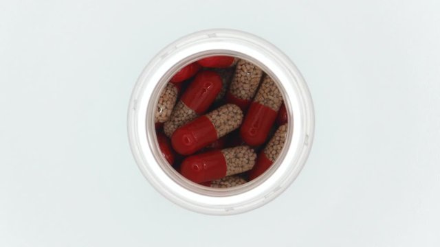 Top View Rotating Of Red Capsules In White Bottle On White Background Close-up.