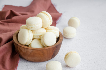 French dessert macaron with vanilla and white chocolate ganache in a wooden bowl on a light stone background. Rustic style. Horazontal orientation. Copy space.