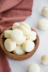 French dessert macaron with vanilla and white chocolate ganache in a wooden bowl on a light stone background. Rustic style. Vertical orientation.