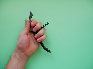 Mens hand holding metal corkscrew on colored background.