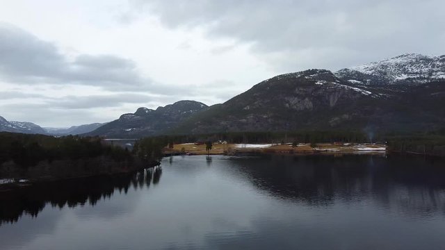 Sliding panoramic aerial view of a mountain lake with the mountain, forest and sky reflecting off the surface of the clear water