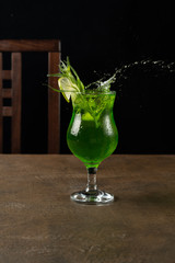 A splash of tarragon lemonade in a glass decorated with a sprig of tarragon and a slice of lime on a dark background
