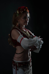 low-key portrait with back light of beautiful woman in traditional folk slavic costume for belly dance holding hands near chest and looking at camera isolated on black