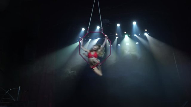 Slim and sexy female Aerial acrobat on the stage with aerial hoop with spot lights on background 