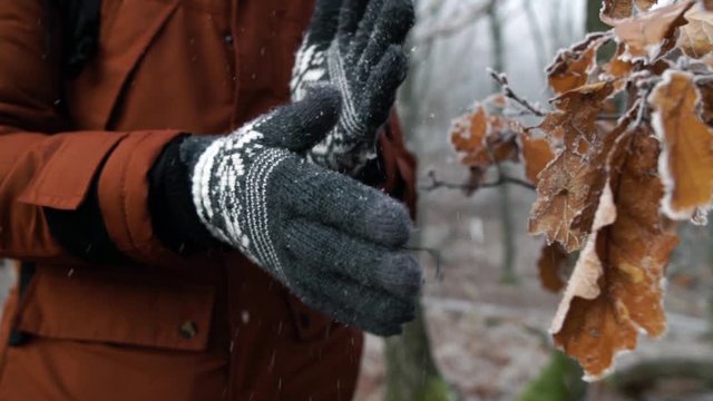 Man shaking of white frost from his gray cotton gloves in forest on cold winter day, SLOW MOTION