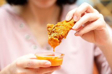 Holding the fried chicken, dip it into the sauce. fast food restaurant.