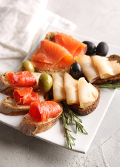 Snack. Bread slices with red and white fish. Olives and rosemary on a white plate. Smoked fish. Black bread and baguette. Background image, copy space