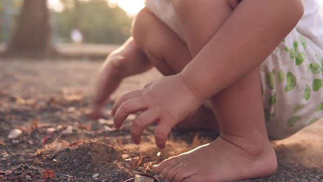 Slow Motion close up video of the hands of a white skin kid playing with dirt with his hands and barefoot at an outdoor park at sunset