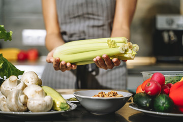 Close up of female hands holding fresh celery in the kitchen. Proper nutrition and health concept