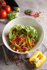 Healthy food. Vegetable salad in a deep light bowl. Tomatoes, peppers, onions, lettuce, eggplant, fork and spices on a light grey background. Background image, copy space
