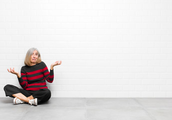 senior or middle age pretty woman shrugging with a dumb, crazy, confused, puzzled expression,...