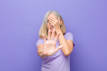 senior or middle age pretty woman covering face with hand and putting other hand up front to stop...