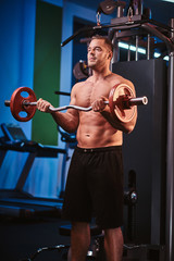 Fit mucular bodybuilder doing weightlifts with barbell in a modern fitness center looking focused