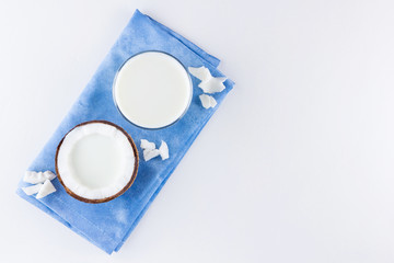 Coconut milk and coconut in glass on white background. Coconut vegan milk non dairy on blue napkin. Healthy drink concept. Minimalism. Alternative milk. Copy space