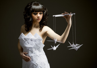 Pensive young girl in an origami dress holds an origami bird in his hands. Puppets on a black...