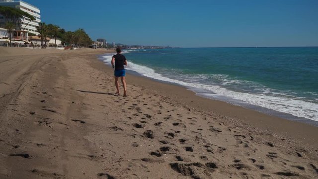Caucasian man running along the beach seen fron behind