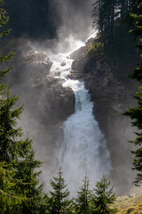 A view of the raging Alpine waterfall shrouded in water fog