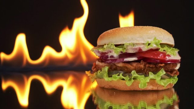 An appetizing and tasty chicken burger on a mirror table, a fire burns in the background.