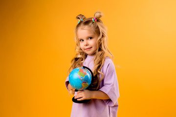 child girl holding a globe and a Notepad for notes, on a yellow background. children's education, space for text