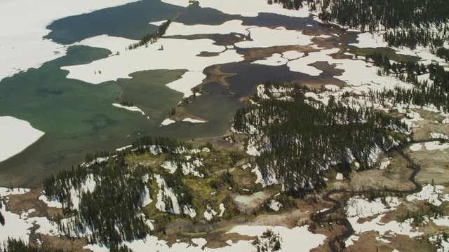 A small stream winds into a mountain lake in Yellowstone National Park, with lingering spring snow