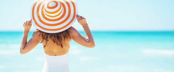 Young woman in hat standing on beach. rear view