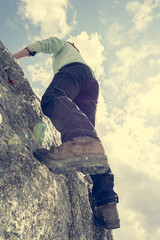 Female mountaineer practicing boulder climbing outdoor on large boulder.