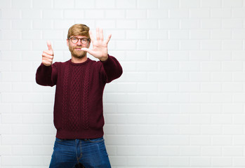 young blonde man smiling and looking friendly, showing number six or sixth with hand forward, counting down agaist vintage tiles wall